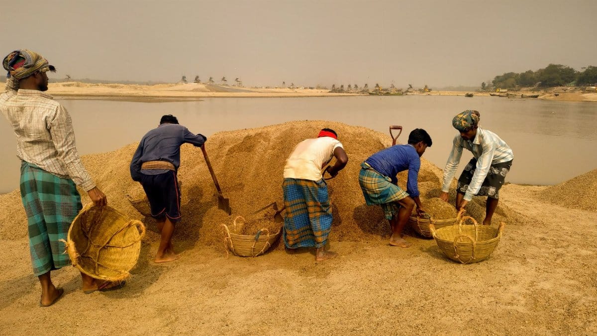 Group of men working with baskets to harvest sand at a riverbank in Bangladesh.