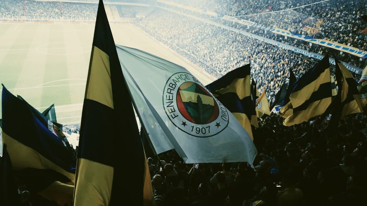 Fans waving Fenerbahce flags in a lively and packed football stadium.