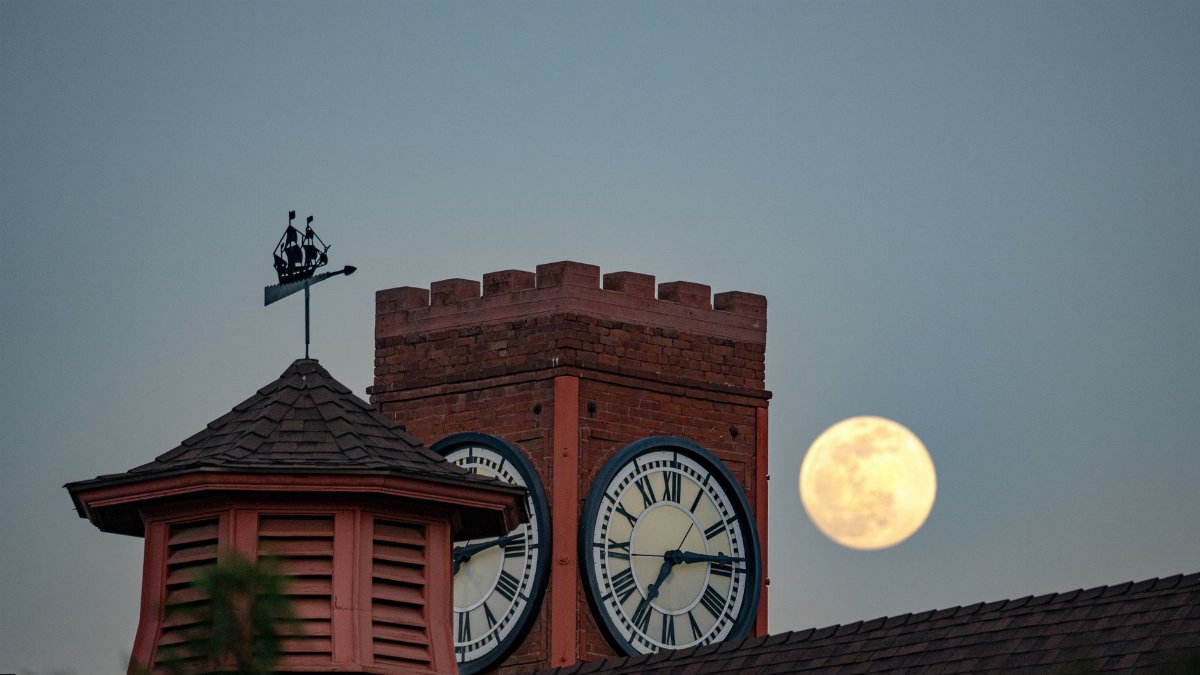 The clock tower in Redlands, CA with a full moon rising behind it at dusk.
