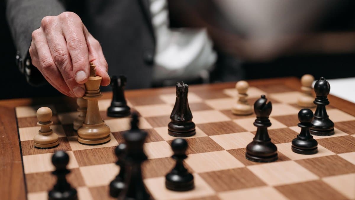 Close-up of a hand making a strategic chess move on a wooden chessboard.