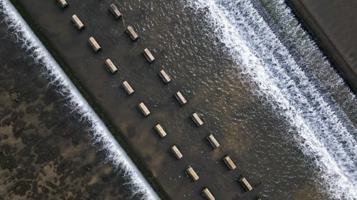 Aerial view of a structured water flow over a weir with rhythmic patterns and concrete blocks.