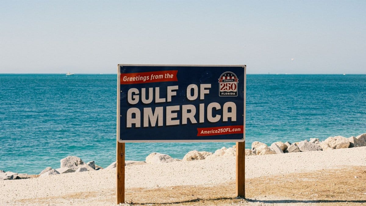 Sign greeting visitors at the Gulf of America beach with clear blue water and rocks.