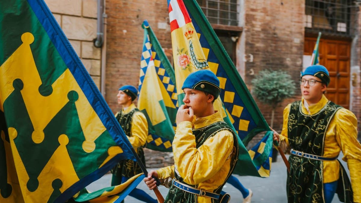 Participants in traditional costumes carry colorful flags in a historic parade, showcasing cultural heritage.
