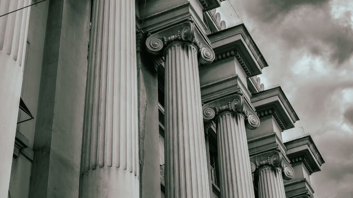 Dramatic grayscale image of Greco-Roman columns against a cloudy sky.