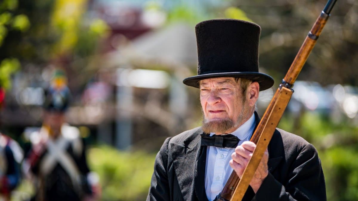 A man in historical attire holding a rifle at an outdoor reenactment event.