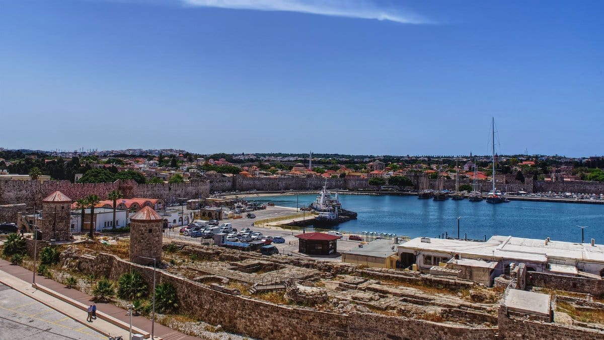 Aerial view of Rhodes Town's historic port and ancient walls under a clear blue sky.