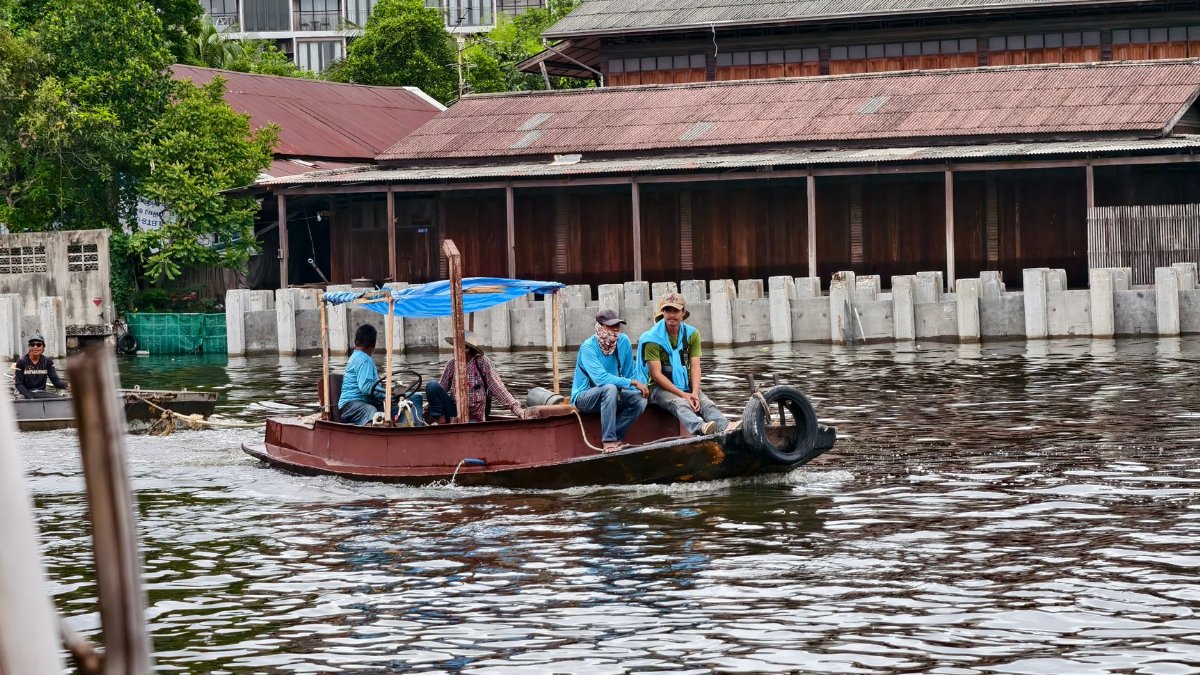Local men steering a small boat along a canal in Bangkok, showcasing everyday life on the water.