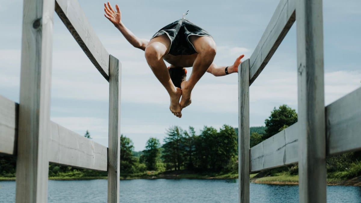 A teenager joyfully jumps off a wooden dock into a serene lake during summer.