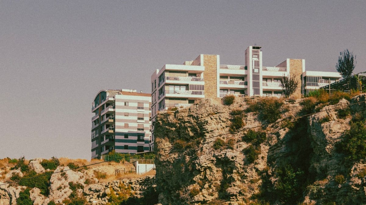 A modern apartment complex perched on a scenic rocky cliff under a clear sky.