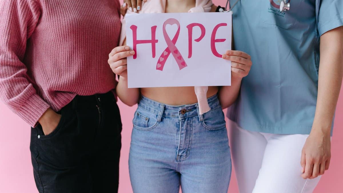 Three women holding a 'HOPE' sign with a pink ribbon for breast cancer awareness.