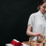 A woman plays chess against an articulated robot, symbolizing AI and human collaboration.