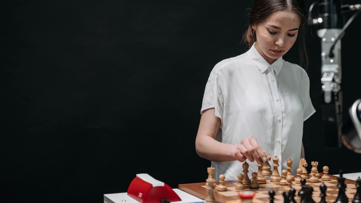 A woman plays chess against an articulated robot, symbolizing AI and human collaboration.
