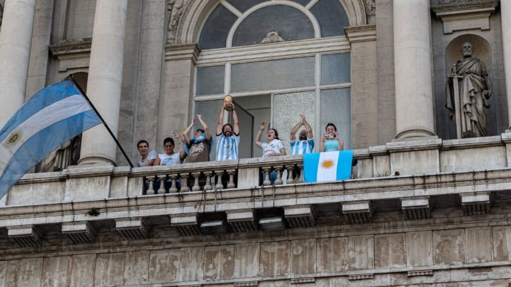 People celebrating with flags and a trophy on a Buenos Aires balcony.