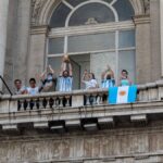 People celebrating with flags and a trophy on a Buenos Aires balcony.