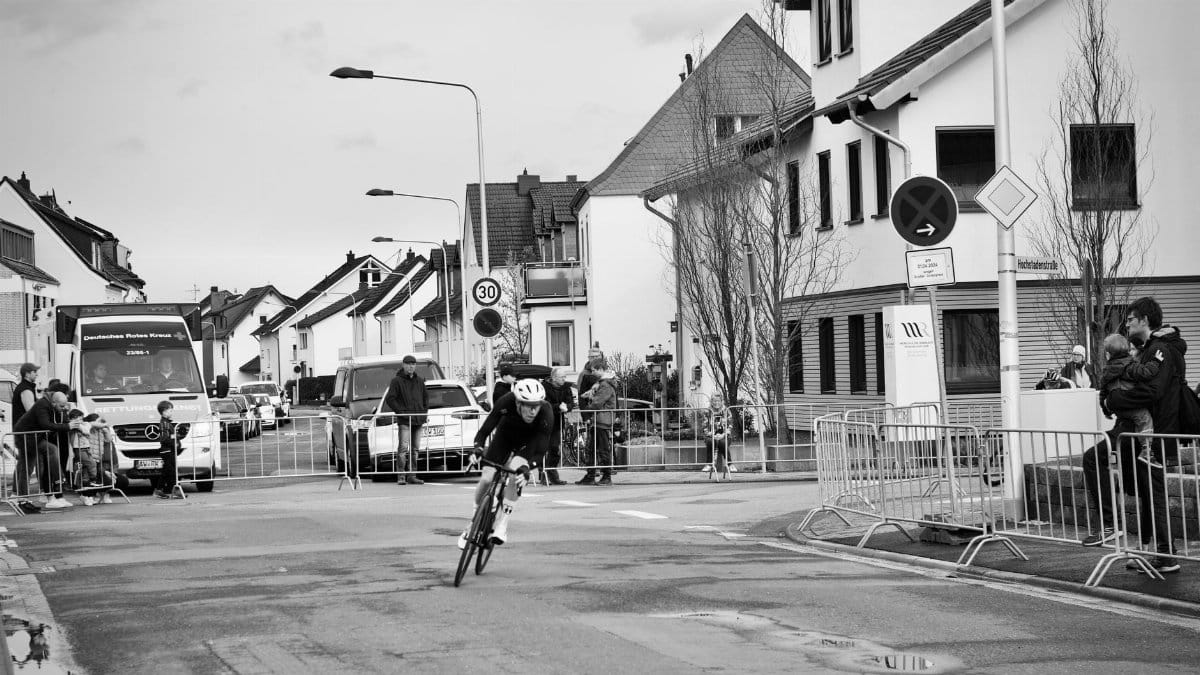 Cyclist competes in urban street race as spectators watch on a cloudy day.