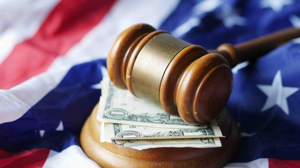 A gavel resting on dollar bills atop the American flag, symbolizing justice and finance.