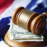 A gavel resting on dollar bills atop the American flag, symbolizing justice and finance.