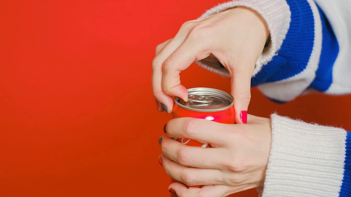 Close-up of hands opening a soda can on a vivid red background, emphasizing the refreshing beverage experience.