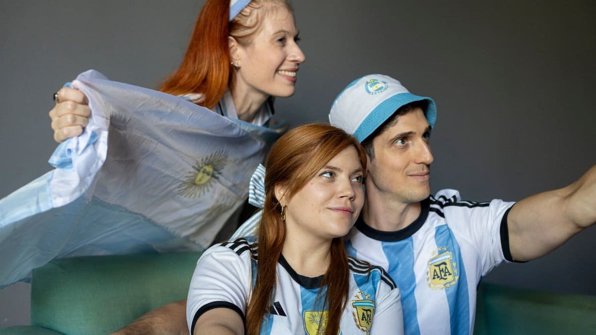 Fans wearing Argentina jerseys cheer while watching a match indoors. Captured in Buenos Aires.
