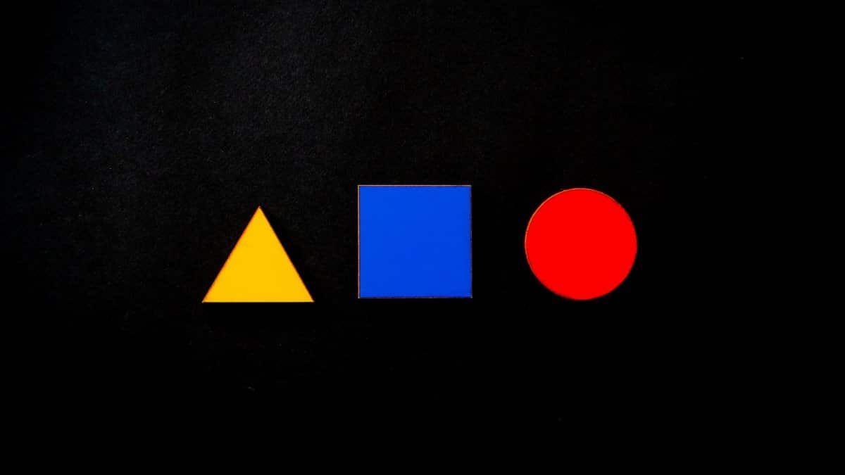 Vivid geometric shapes of triangle, square, and circle in primary colors on a black background.