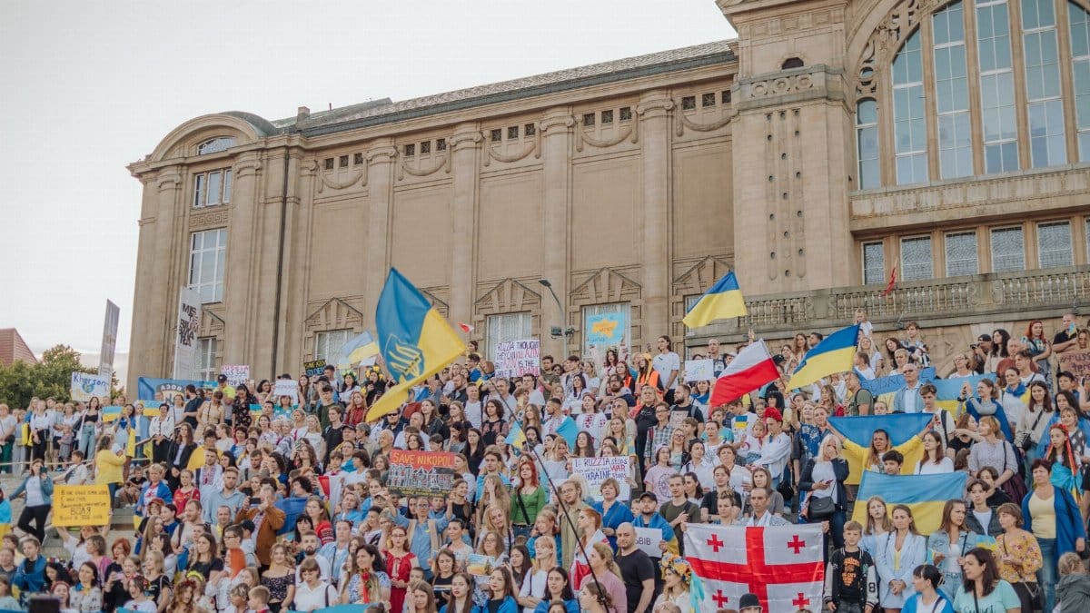 A vibrant crowd gathers in Szczecin, Poland for a public demonstration waving various national flags.