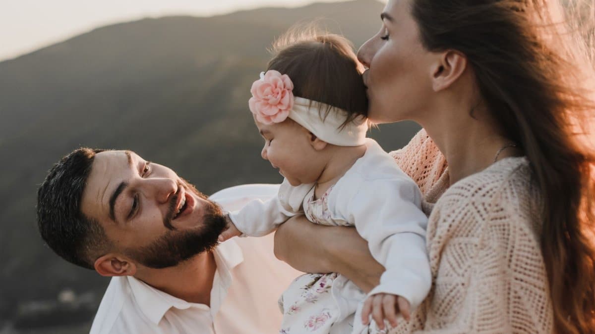 A joyful family moment with parents and baby enjoying the outdoors at sunset.
