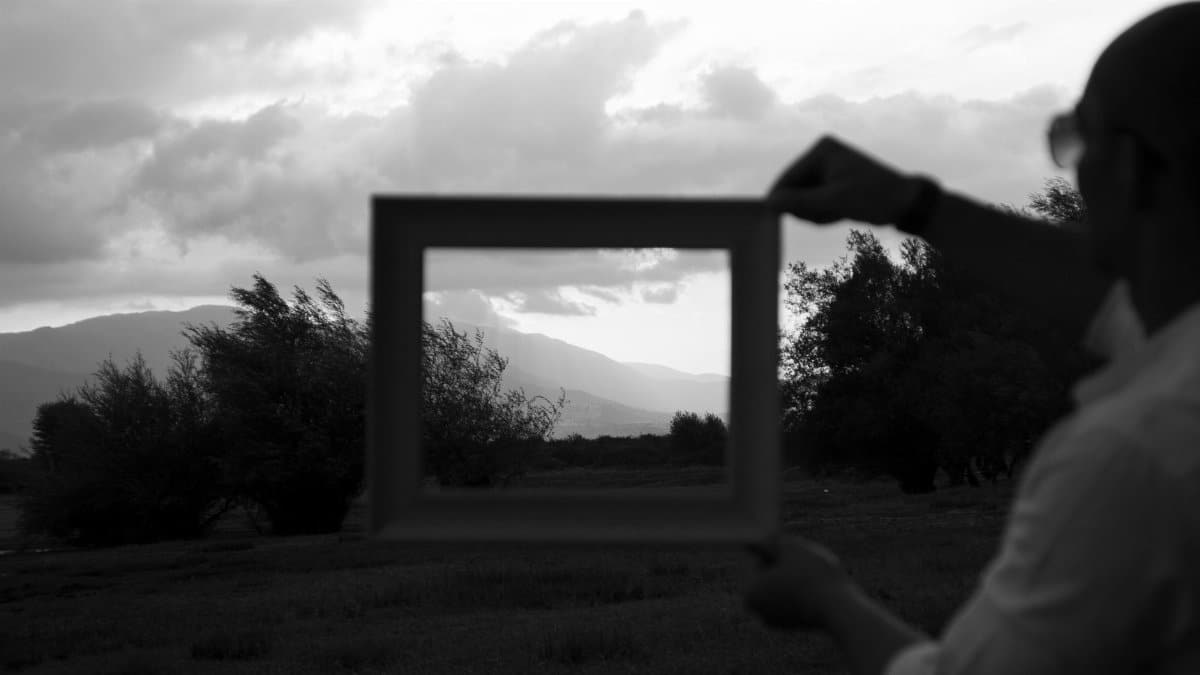 A creative black and white landscape with a focus on mountains framed by a person holding an empty frame.