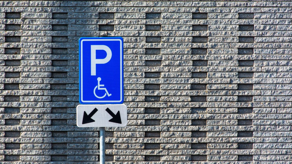 A disability parking sign stands against a textured brick wall background.