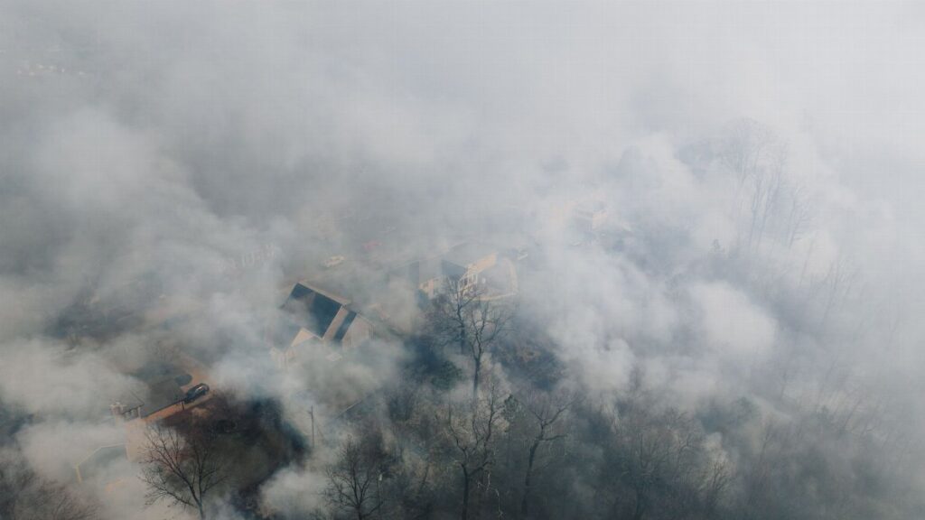 Aerial shot of a neighborhood shrouded in smoke, obscuring houses and trees.