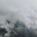 Aerial shot of a neighborhood shrouded in smoke, obscuring houses and trees.