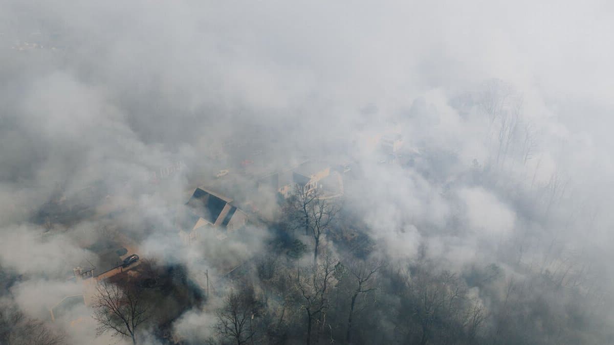Aerial shot of a neighborhood shrouded in smoke, obscuring houses and trees.