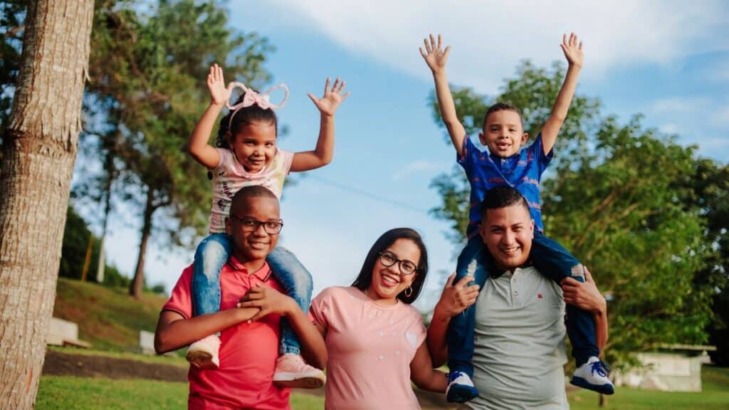 A joyful family spending quality time outdoors with kids on parents' shoulders.