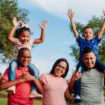A joyful family spending quality time outdoors with kids on parents' shoulders.