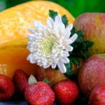 Vibrant still life of apples, strawberries, starfruit, and a chrysanthemum on a dark fabric backdrop.