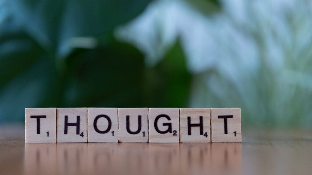 Wooden blocks spelling 'THOUGHT' on a table with a blurred background, conveying ideas and introspection.