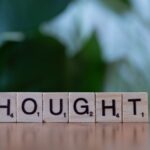 Wooden blocks spelling 'THOUGHT' on a table with a blurred background, conveying ideas and introspection.