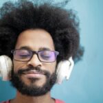 A joyful man with afro hair enjoying music with headphones, eyes closed, and a smile.