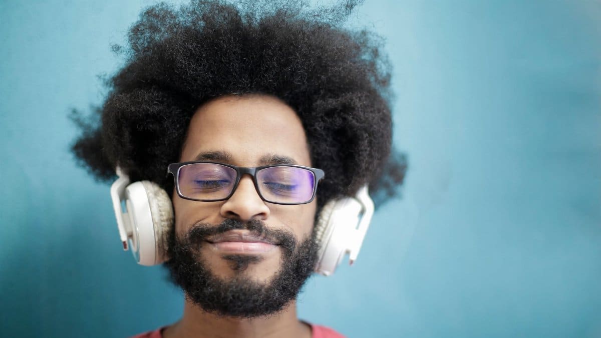 A joyful man with afro hair enjoying music with headphones, eyes closed, and a smile.