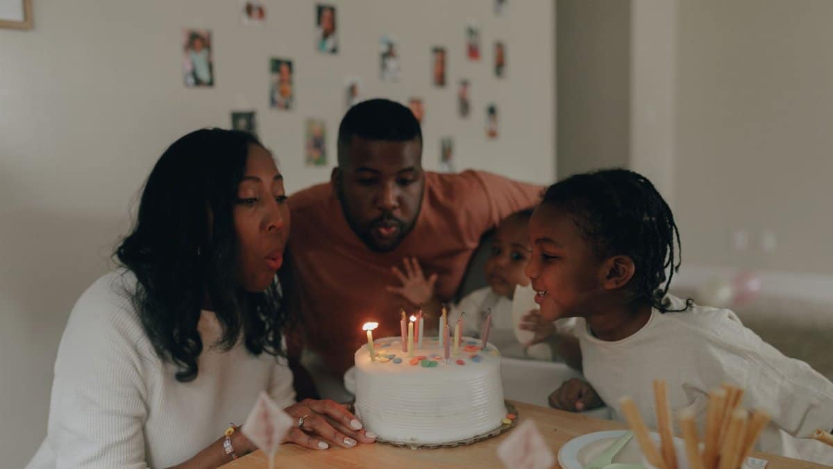 A joyful family moment as parents and children blow out birthday candles on a cake indoors.