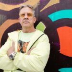 A confident senior man in bright attire poses against vibrant street art, exuding style.