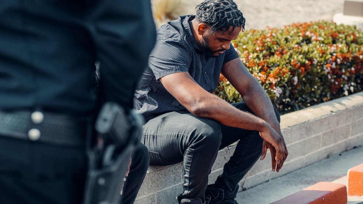 A police officer watches over a seated suspect outdoors, conveying law enforcement dynamics.