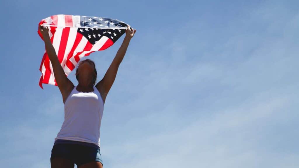 Woman celebrating Independence Day with American flag under a clear blue sky.