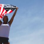Woman celebrating Independence Day with American flag under a clear blue sky.