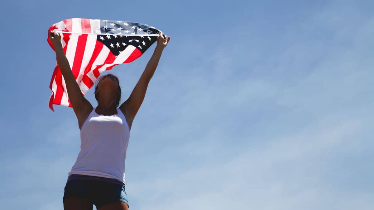 Woman celebrating Independence Day with American flag under a clear blue sky.