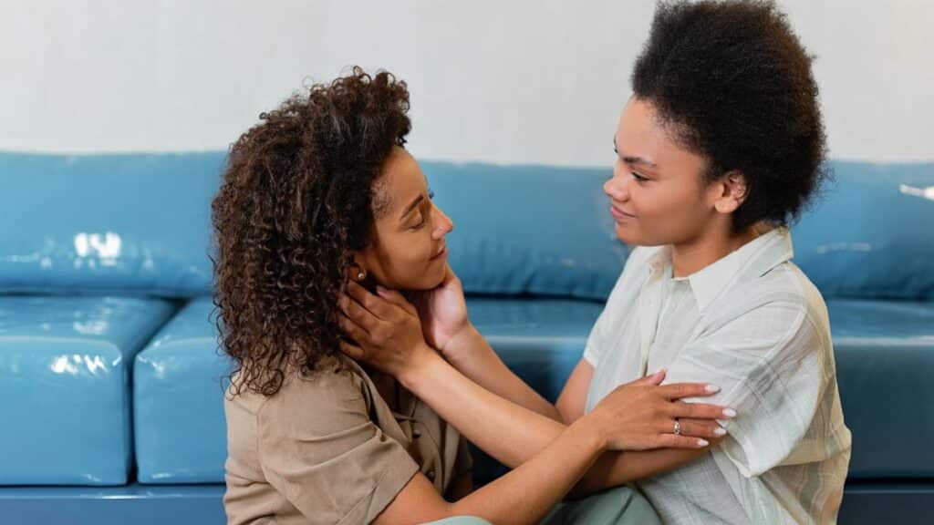 Two women embracing lovingly on a blue sofa, showcasing affection and connection.