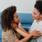 Two women embracing lovingly on a blue sofa, showcasing affection and connection.