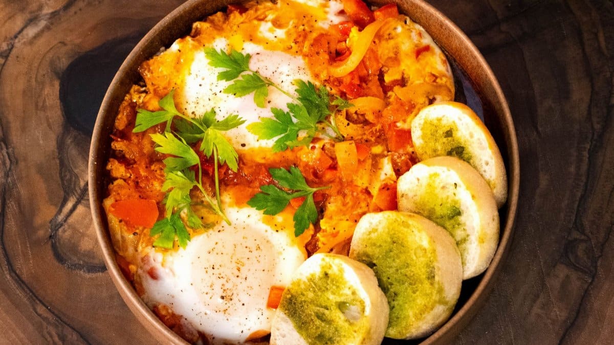 A hearty shakshuka with poached eggs, fresh herbs, and bread slices, perfect for a flavorful meal.
