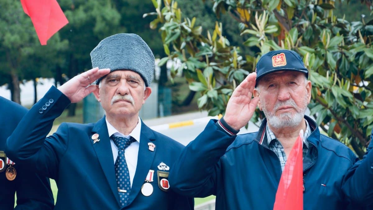 Two elderly veterans in uniform salute during an outdoor ceremony in Balıkesir, Türkiye.
