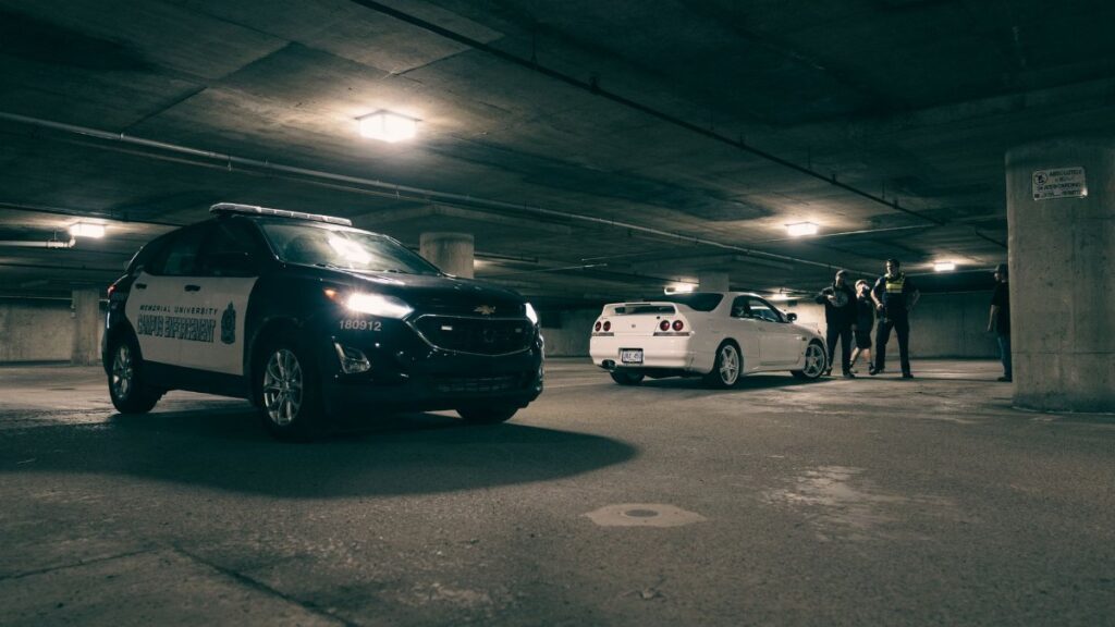 Police vehicles and a group of people in an underground parking lot. Dramatic lighting sets the scene.