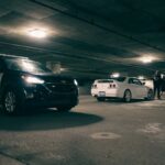 Police vehicles and a group of people in an underground parking lot. Dramatic lighting sets the scene.
